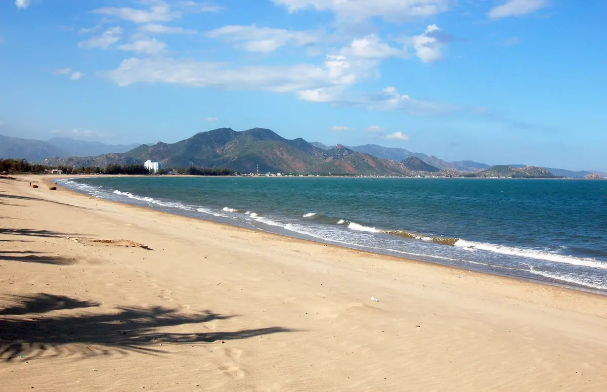 Curved pale sand beach with surf and a mountain range behind