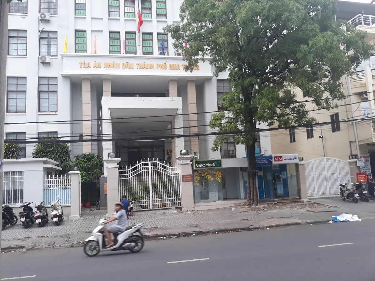 White court building with columns at the entrance, a tree in front and a scooter passing on the road