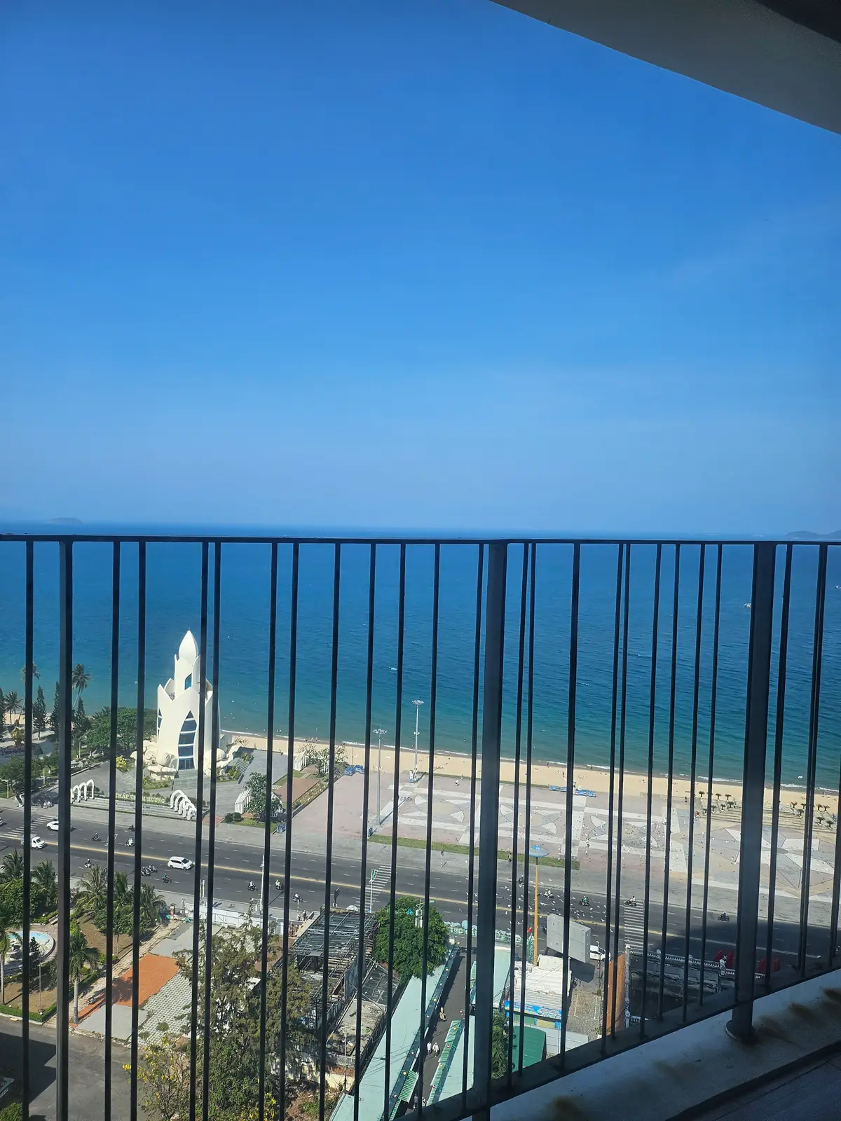 Balcony railing in front of a blue sea with a white tower and the shoreline below