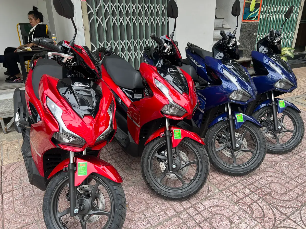Four scooters in red and blue parked in a row on a tiled pavement
