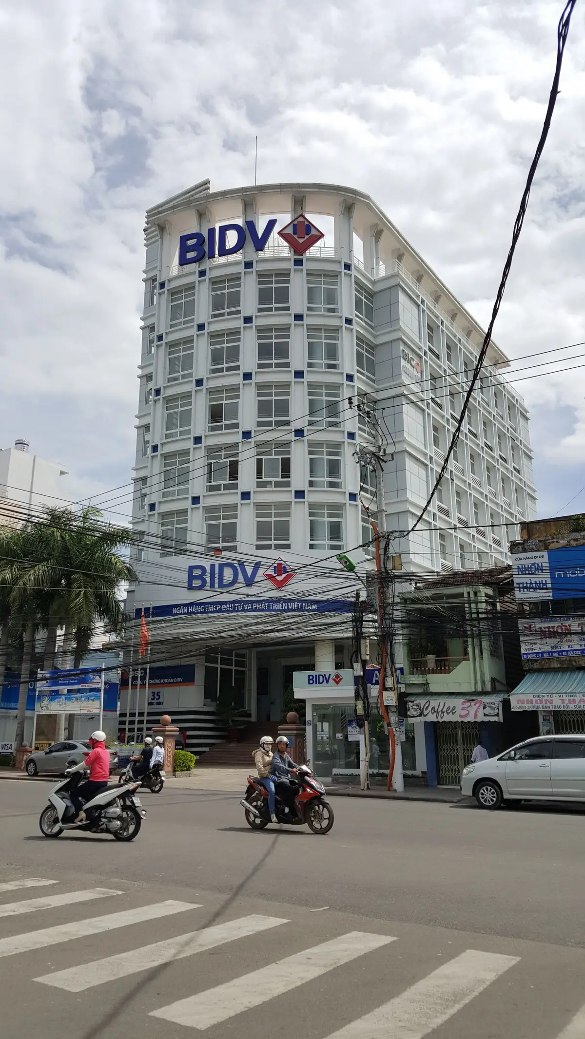White multi-storey BIDV bank building seen from the street with the blue bank sign above the ground floor.
