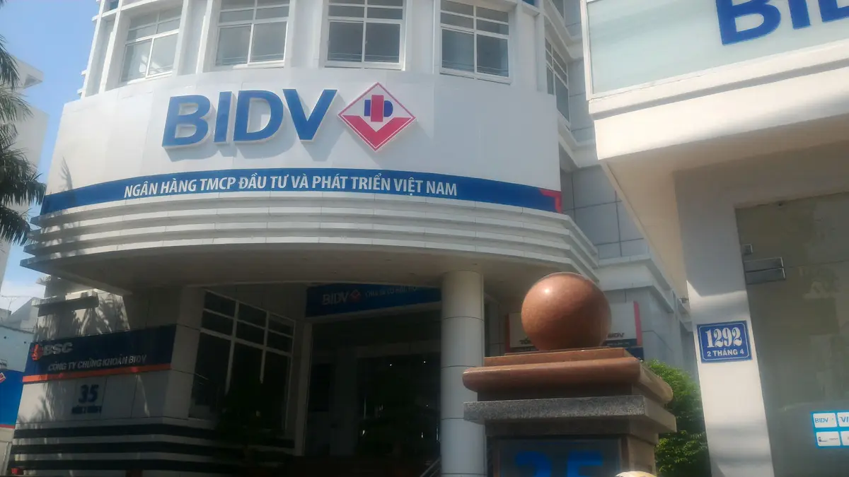 Curved facade of the BIDV branch with the blue bank sign and a house number on the wall to the right.