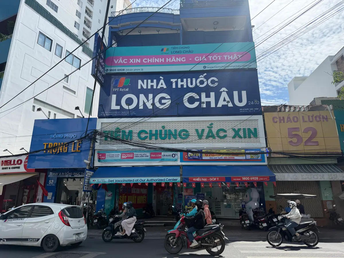 A street shopfront with a blue Long Chau pharmacy sign above a vaccination sign.