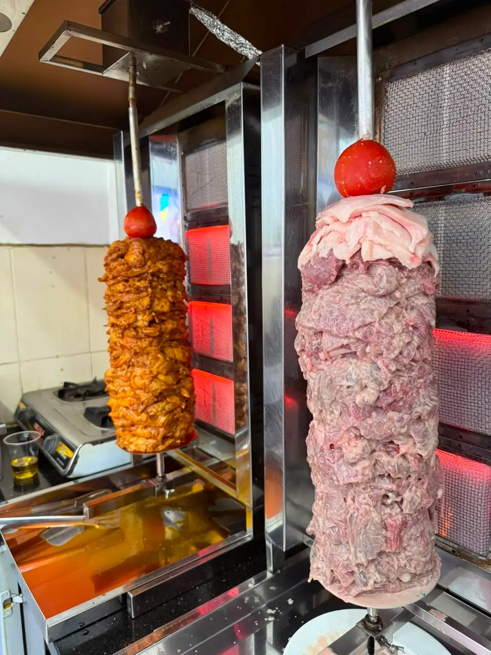 Two vertical doner spits, one cooked and one raw, in a kitchen