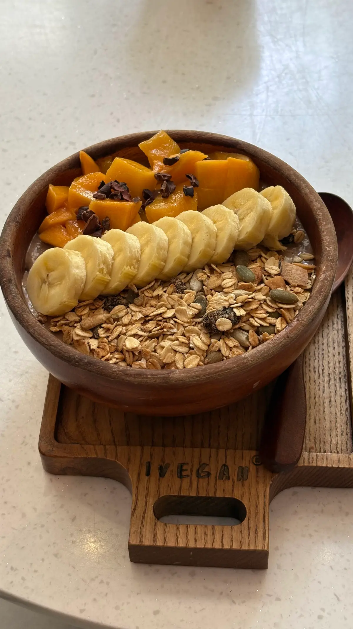Wooden bowl of granola topped with sliced banana