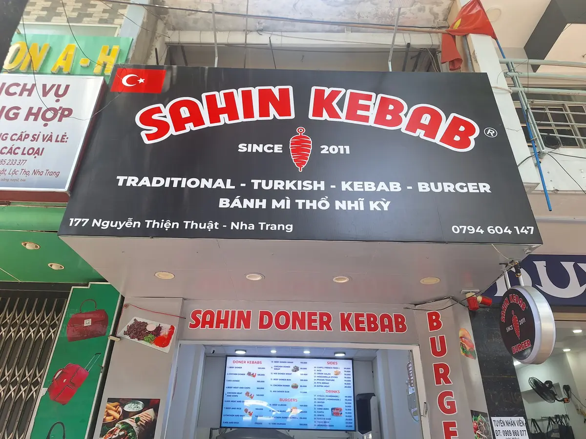 Red Sahin Kebab sign above a narrow shopfront with a menu screen