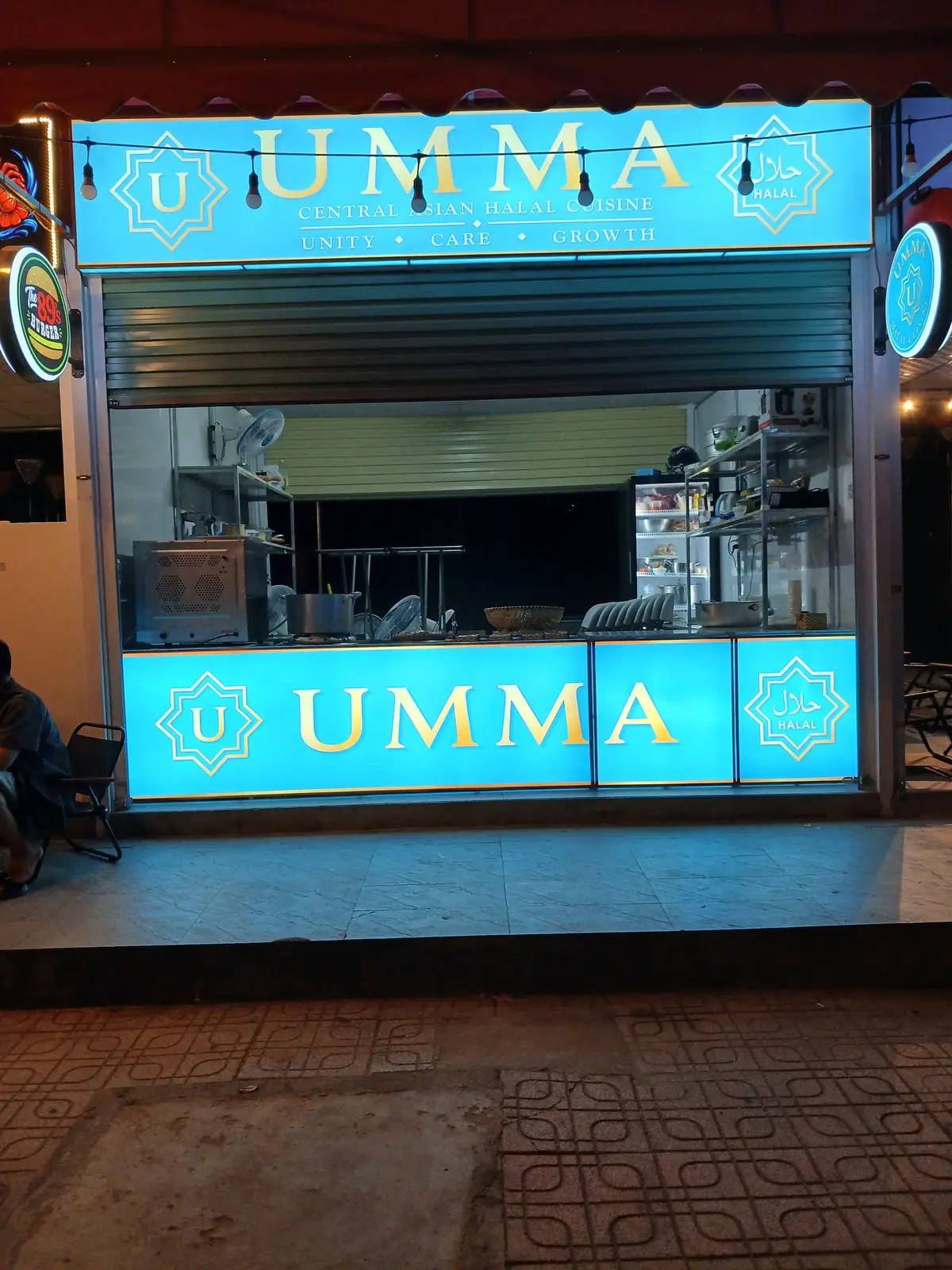 Blue lit counter with the UMMA name above a small open kitchen