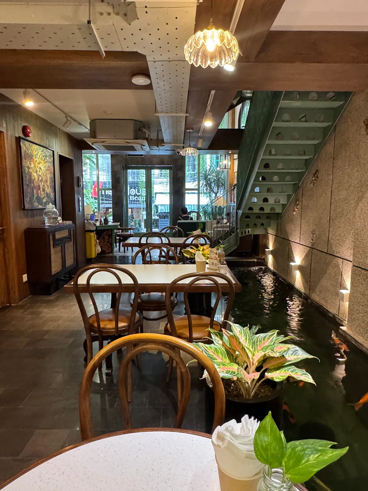 Cafe interior with wooden chairs beside an indoor koi pond lit by wall lights