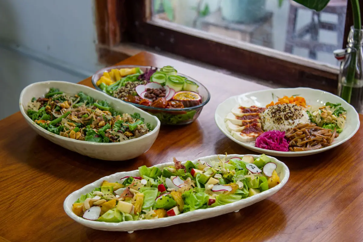 Four oval bowls of colourful salads on a wooden counter