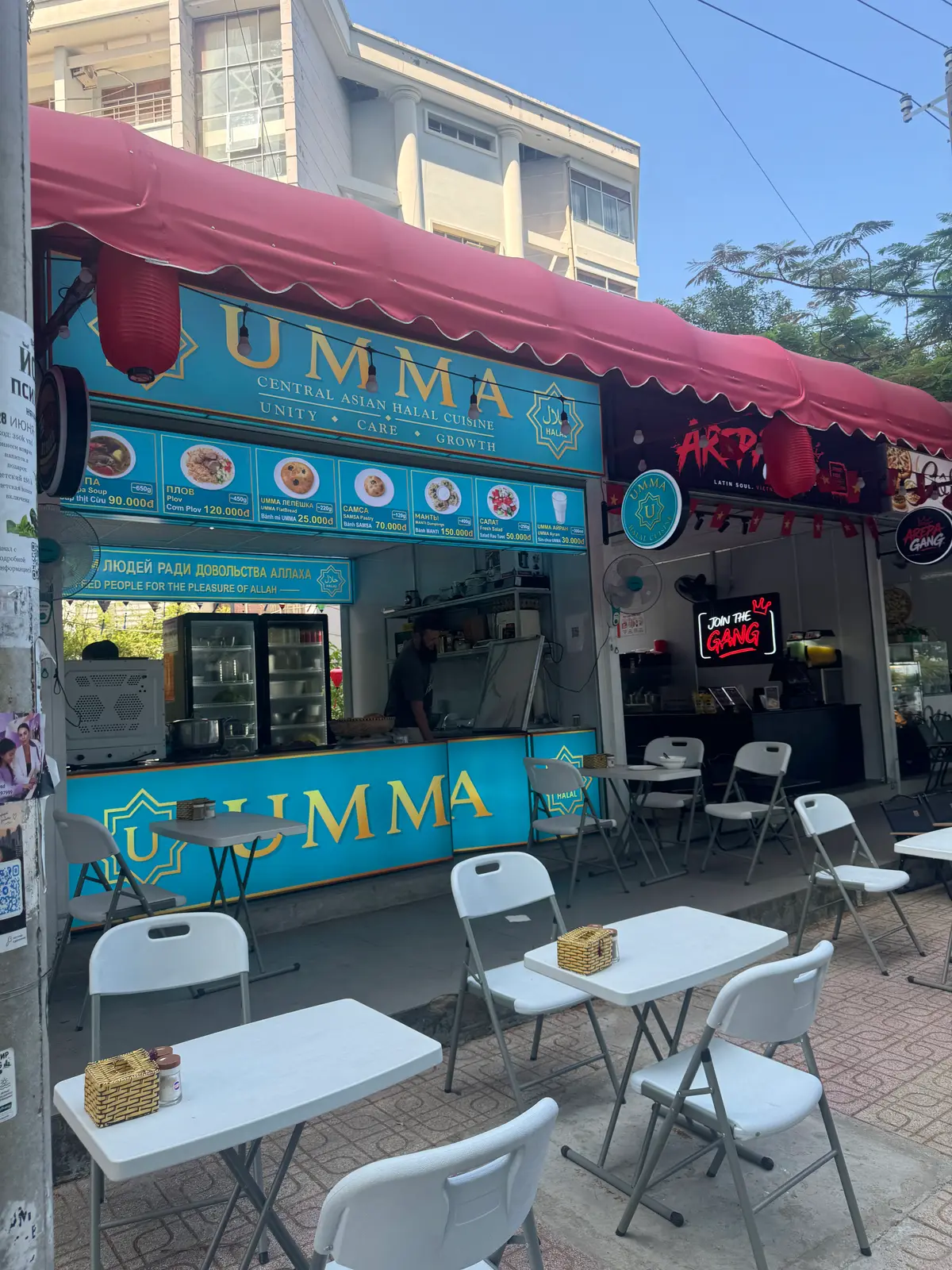 Small blue-fronted food stall with plastic chairs and a menu board