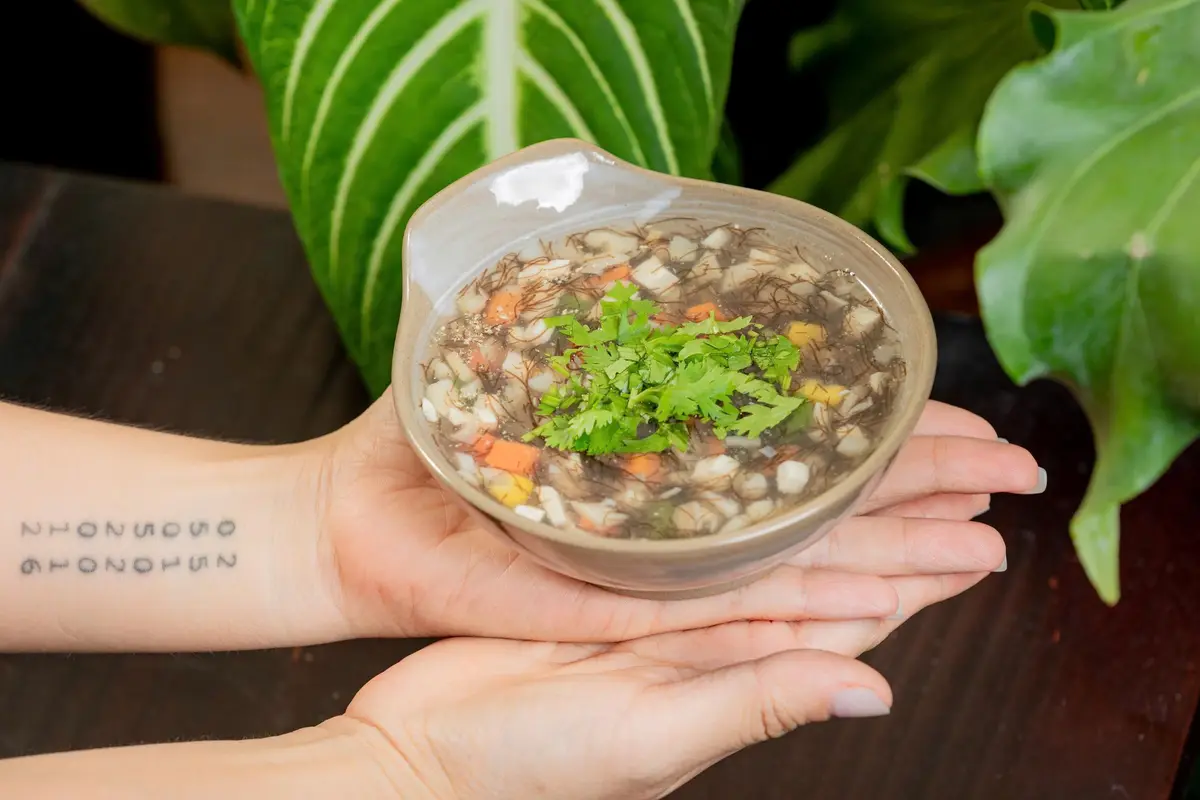 Hands holding a small bowl of mushroom porridge garnished with herbs