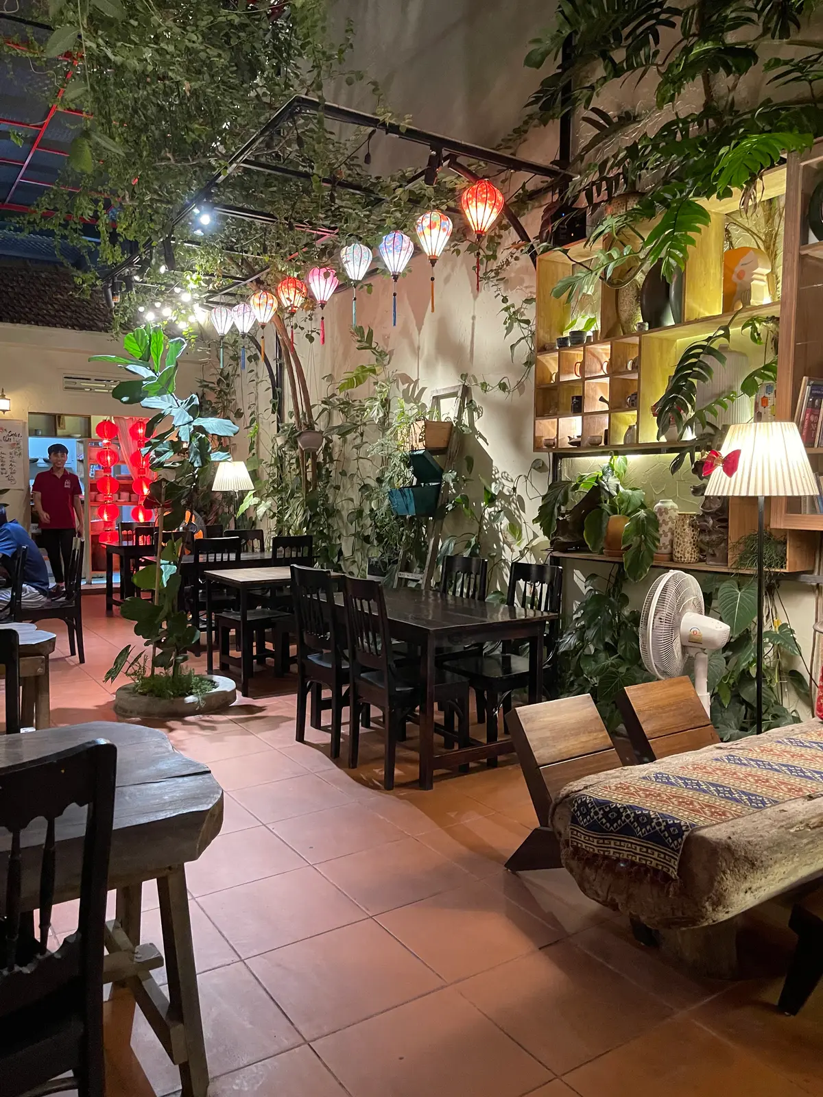 Leafy courtyard dining room with wooden tables, table lamps and hanging plants