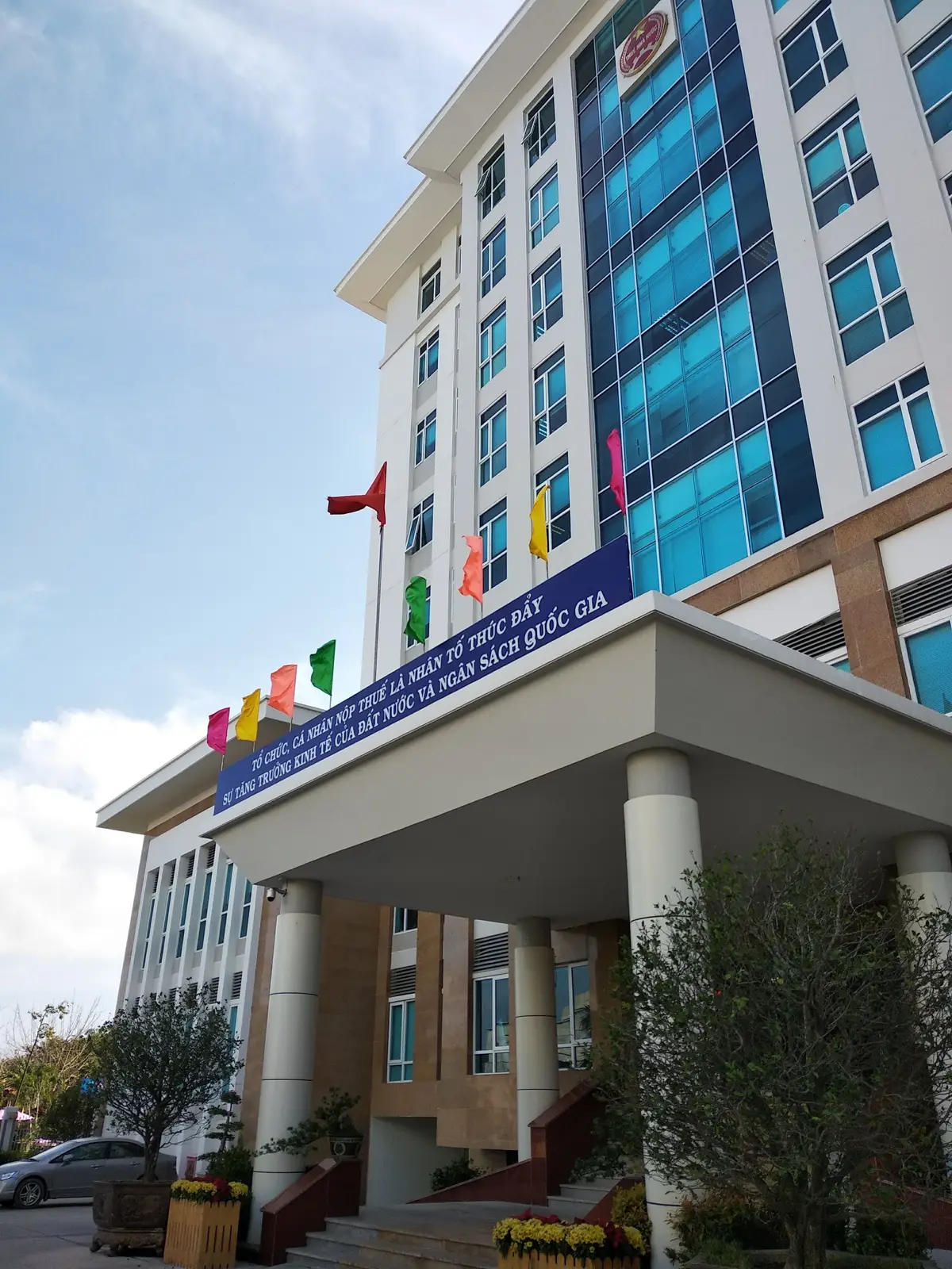 Entrance of a large office building with a canopy, flags and a banner above the doorway.
