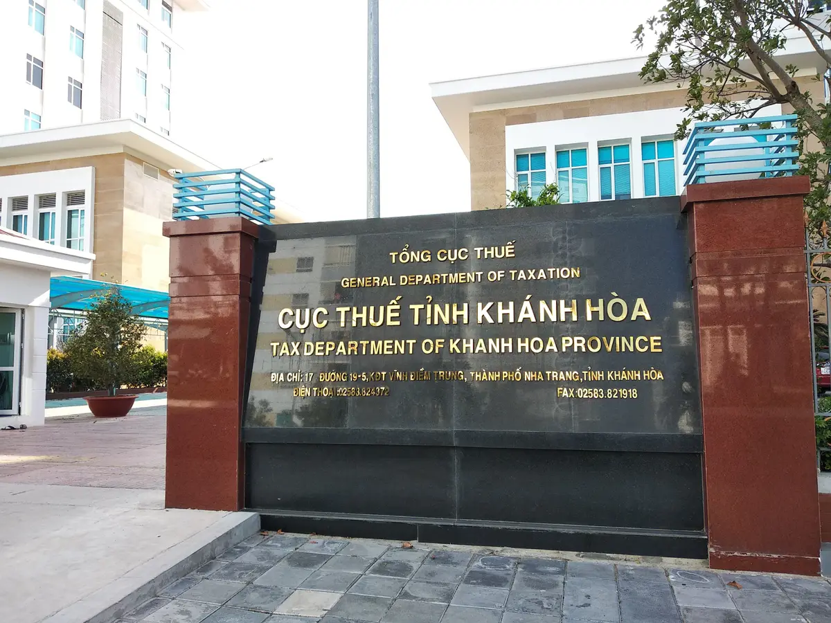 Granite entrance sign reading Tax Department of Khanh Hoa Province in Vietnamese and English, with a landscaped courtyard behind.