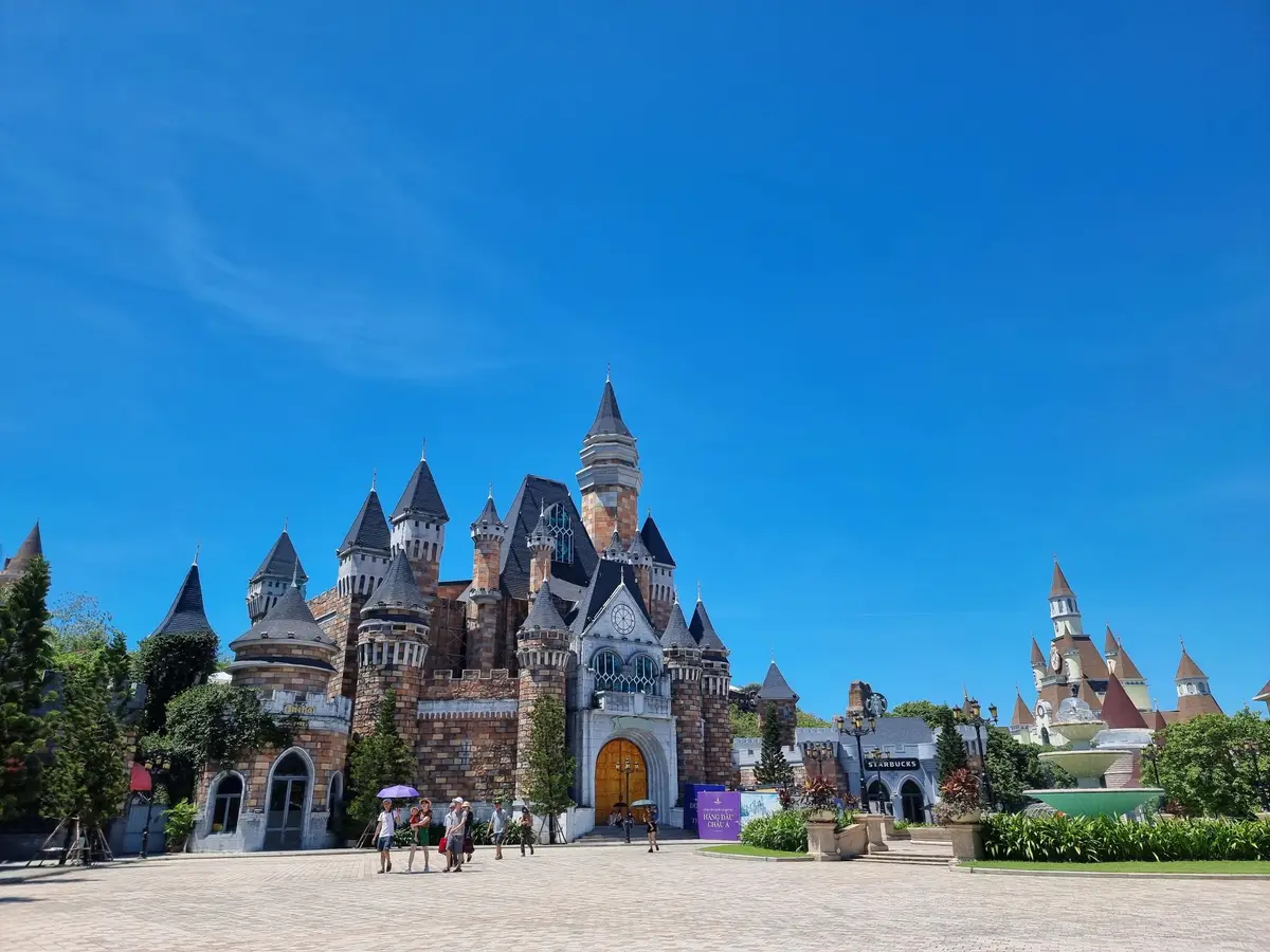 Fairy-tale castle buildings with pointed towers in an open stone square under a blue sky