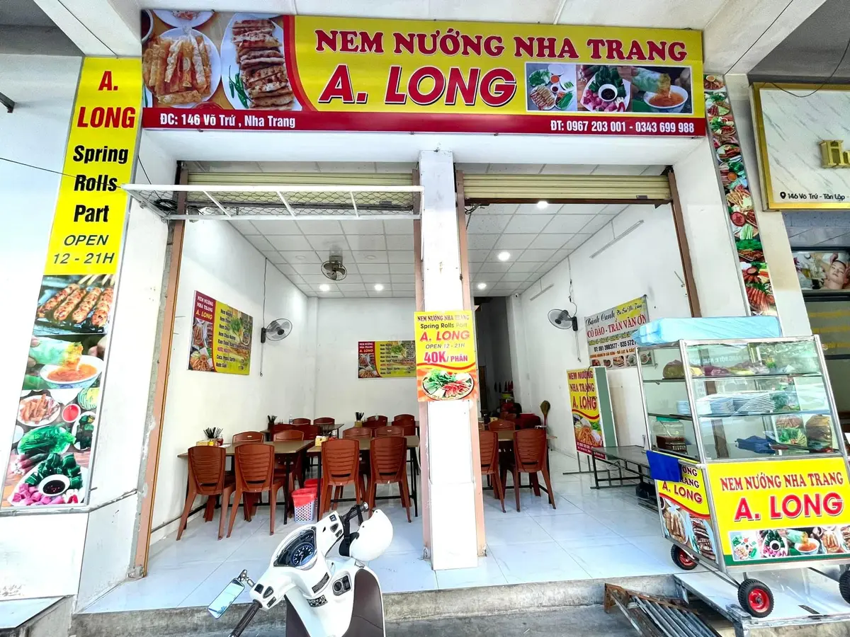 Shopfront with a yellow and red banner and a spring rolls sign above wooden tables