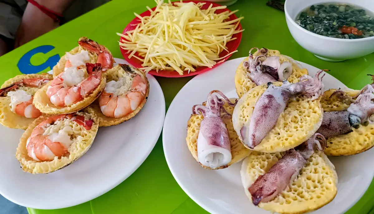 Plates of small rice pancakes topped with shrimp and squid, with shredded green papaya
