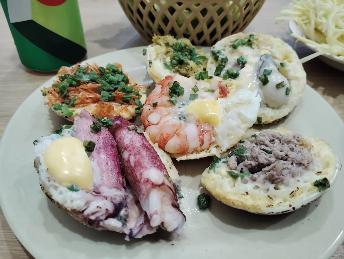 Plate of small pancakes topped with whole prawns, squid, egg yolk and spring onion