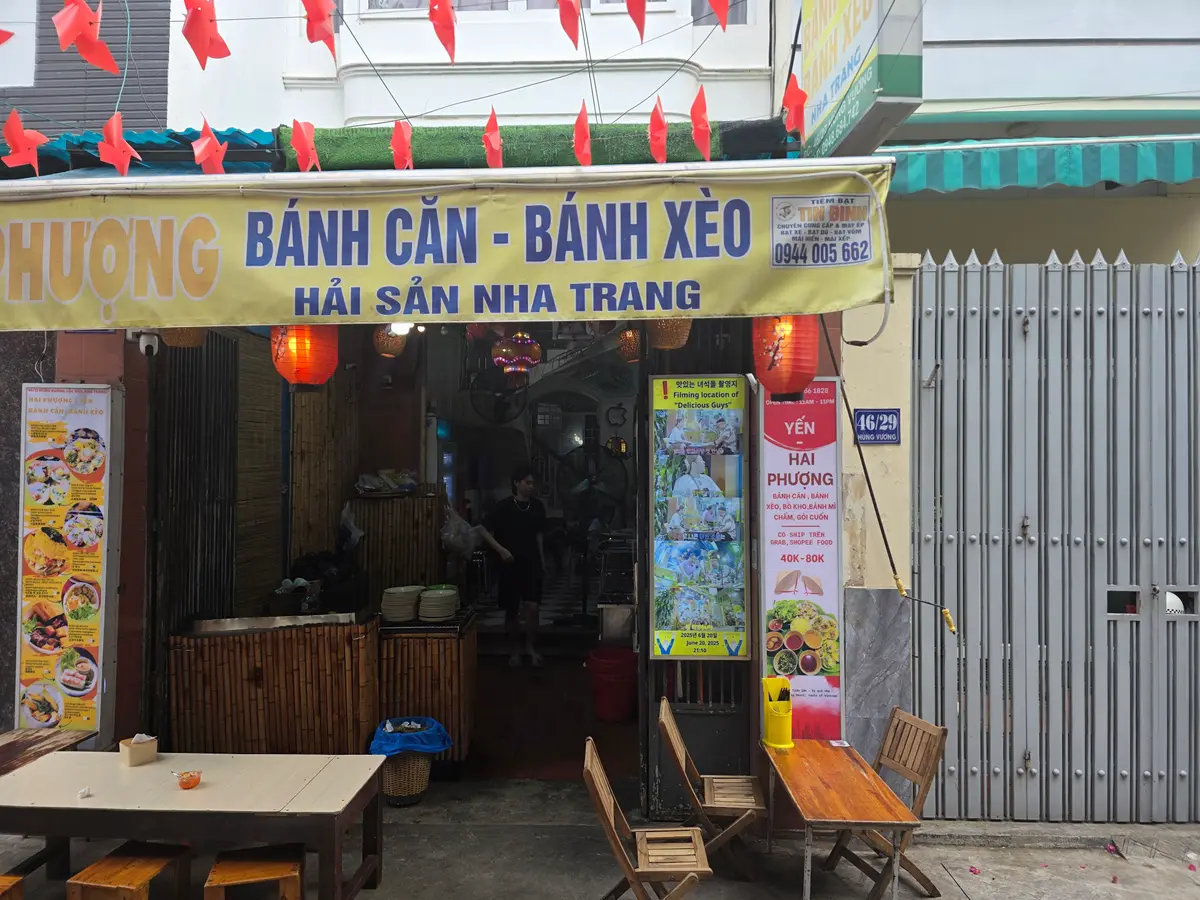 Alley shopfront with a yellow sign, red lanterns and wooden tables