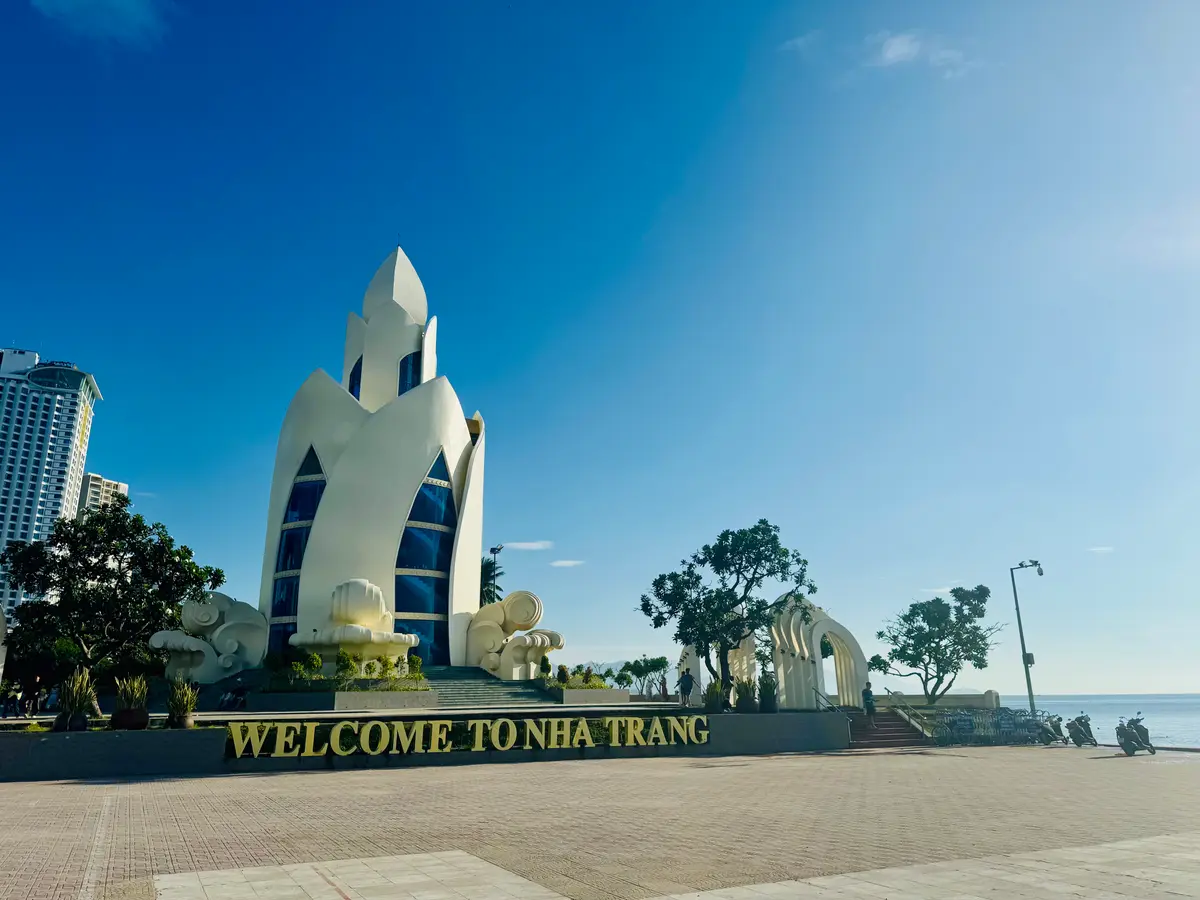 White lotus-shaped monument with a Welcome to Nha Trang sign on the seafront promenade, with high-rise hotels behind