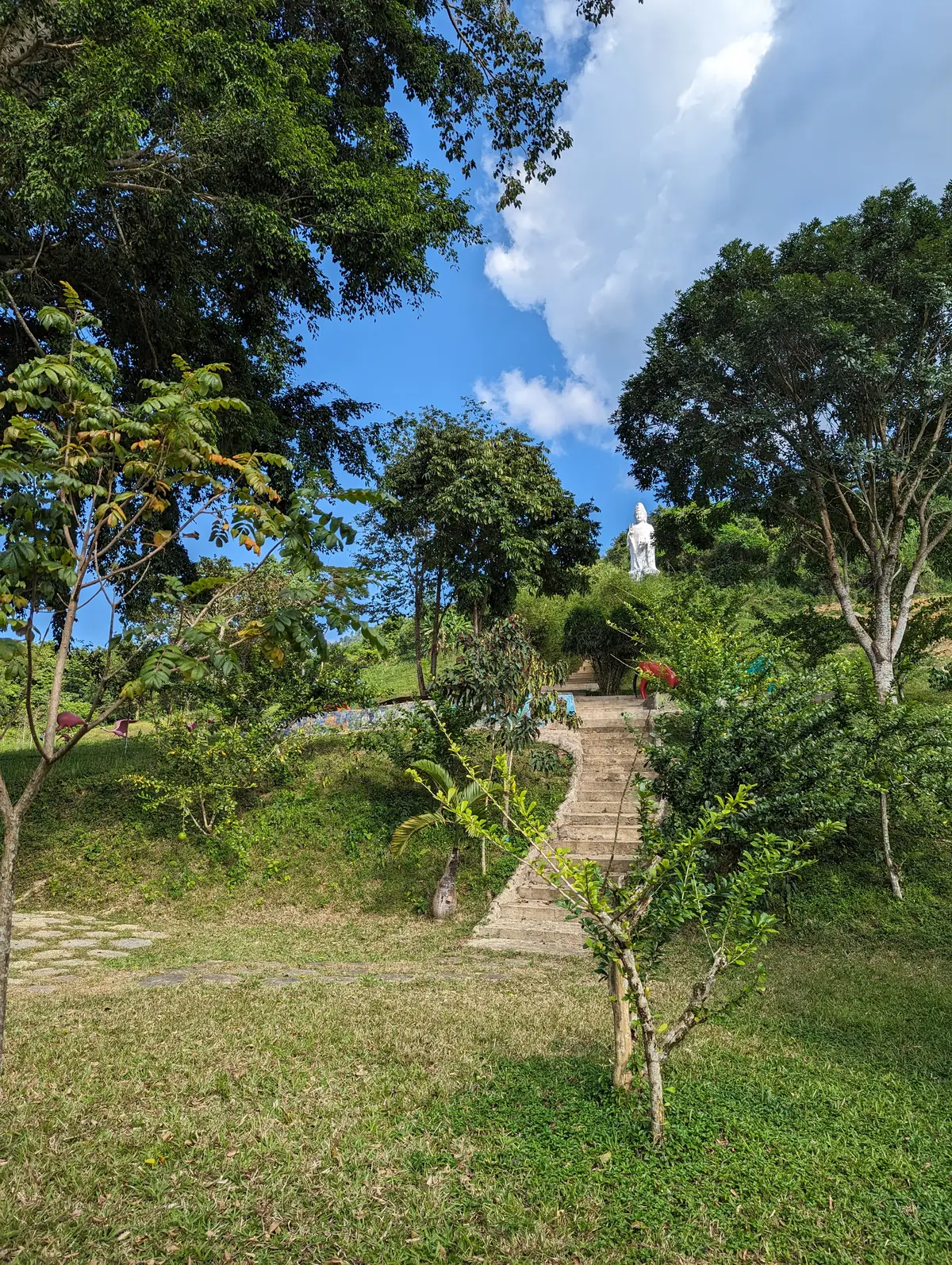 Stone steps climbing a green hillside towards a white statue