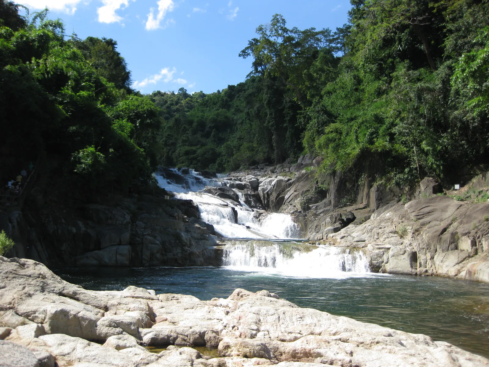 Small waterfall tumbling over pale rocks into a pool in a forested valley